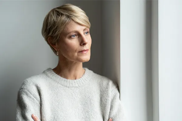 A blond, middle-aged woman looks out the window with a tired expression. Get chronic fatigue treatment from Morgan Burns, APRN in New Smyrna Beach.