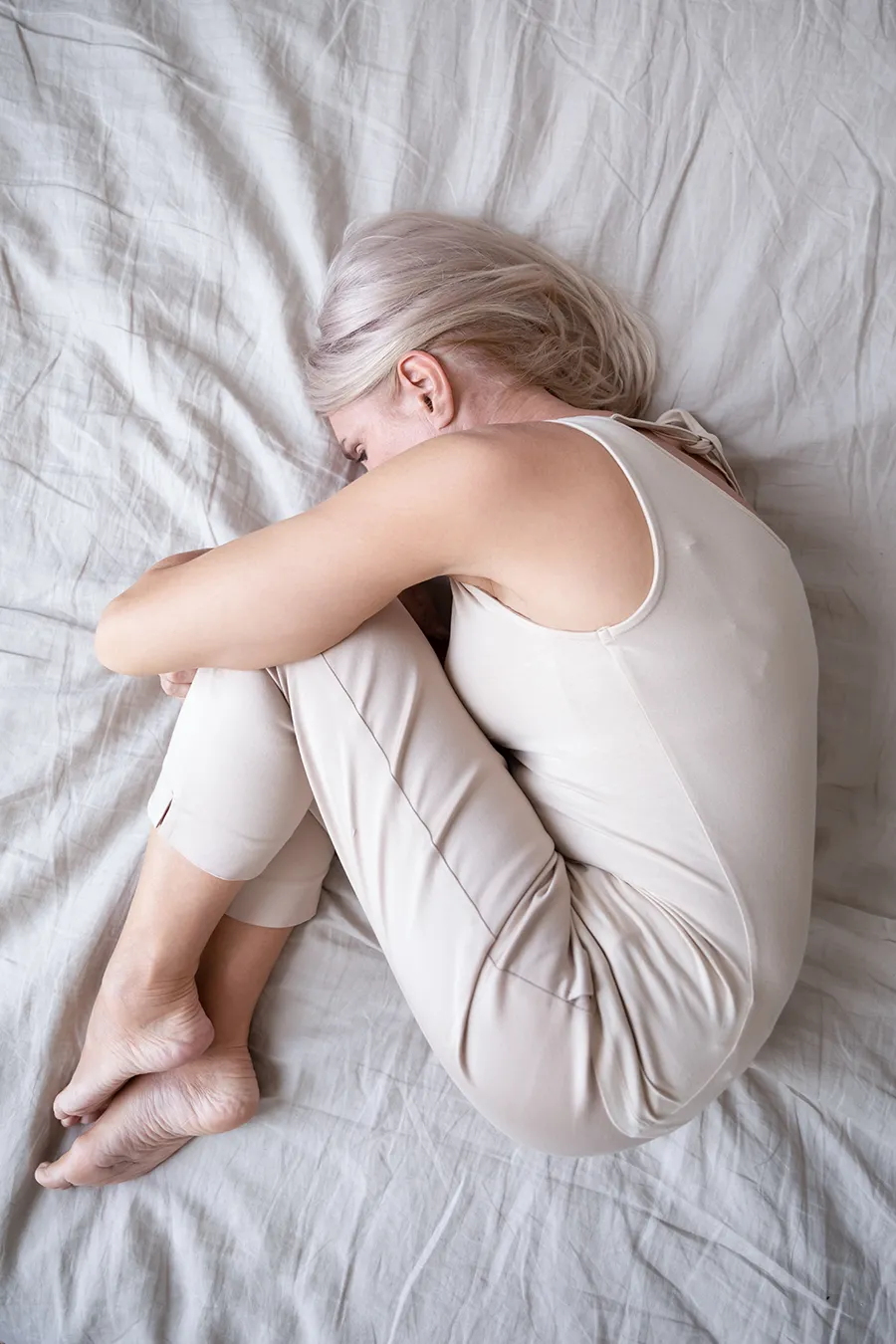 A woman curled up on a bed. Get depression treatment from Morgan Burns, APRN in New Smyrna Beach.