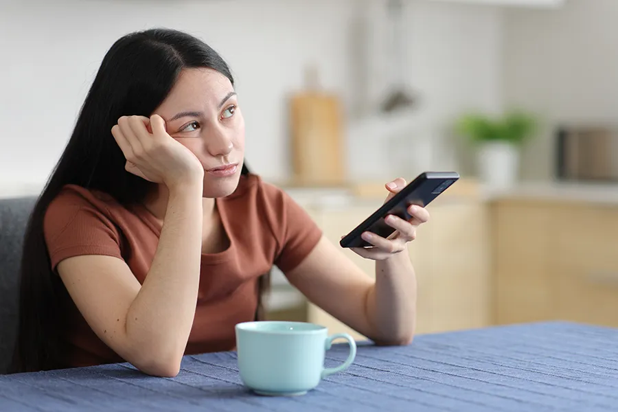 A woman stares into space with her phone in hand. Get treatment for focus issues from Morgan Burns, APRN in New Smyrna Beach.