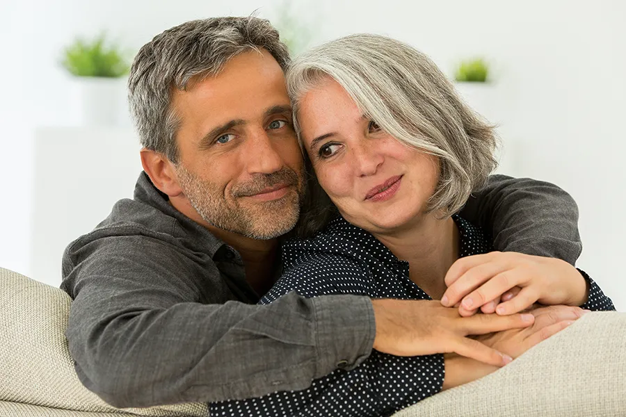 A middle-aged couple holding each other on the couch. Get Hormonal and Vitality Peptide Treatment from Morgan Burns, APRN in New Smyrna Beach.