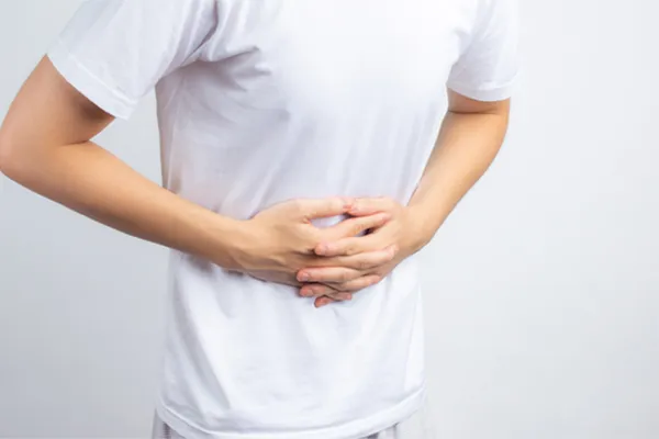 A person holding their stomach in visible discomfort against a plain background. Morgan Burns, APRN treats irritable bowel syndrome with functional medicine in New Smyrna Beach.