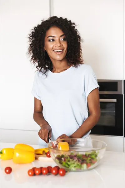 Image featuring a smiling woman chopping vegetables for a salad in a bright, white kitchen. Morgan Burns, APRN offers Irritable Bowel Syndrome Treatment and Digestive Support in New Smyrna Beach.