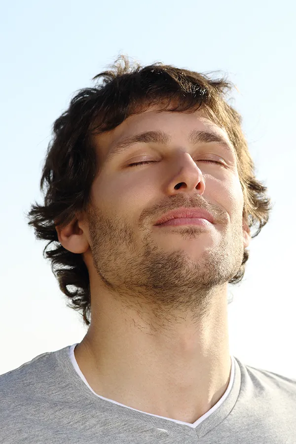 A brown-haired man closes his eyes and breathes in fresh air with his face turned up to the sky. Get treatment for Lupus from Morgan Burns, APRN in New Smyrna Beach.