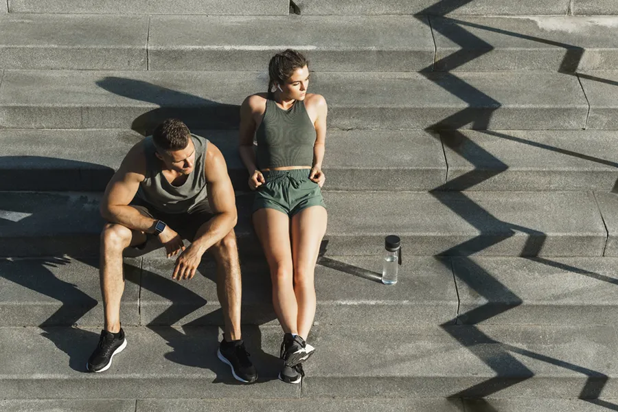 A couple in gray and green track clothes resting after a workout on stone steps, happy with their weight loss plans from Morgan Burns, APRN in New Smyrna Beach.
