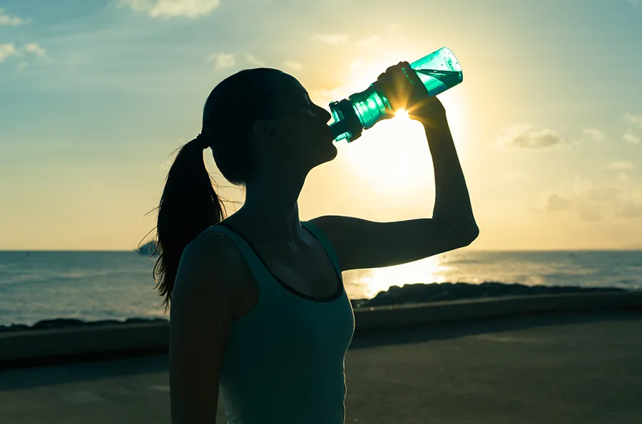 A woman hydrates during a beach run at sunset. Schedule natural detoxification treatment from Morgan Burns, APRN in New Smyrna Beach.