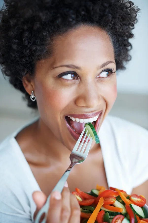 A Black woman smiles while eating a healthy salad. Get natural detoxification treatment from Morgan Burns, APRN in New Smyrna Beach.