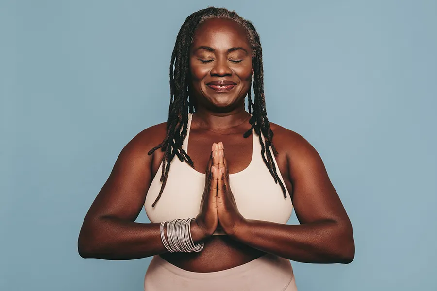 An older black woman with closed eyes holds her hands together in a yoga pose. Get treatment for pre-diabetes from Morgan Burns, APRN in New Smyrna Beach.