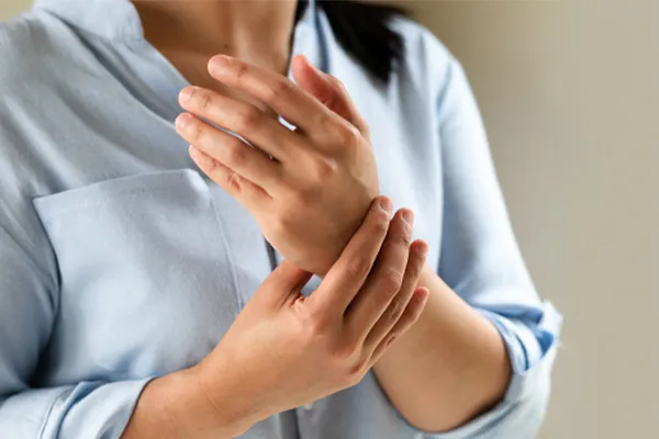 Close up of a woman in a blue blouse rubbing her wrist. Get rheumatoid arthritis treatment from Morgan Burns, APRN in New Smyrna Beach.