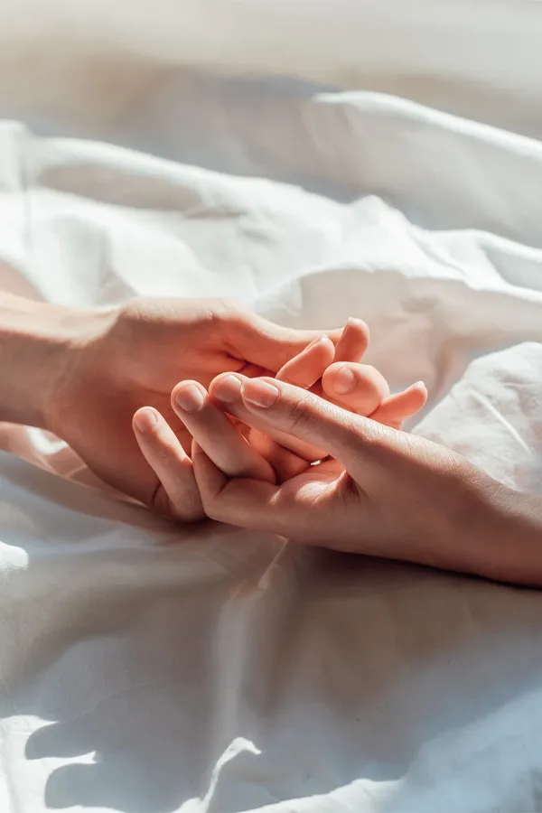 A close up of a man and woman's hands lightly clasping on a bedsheet, representing successful sexual health peptide therapy for men and women by Morgan Burns, APRN in New Smyrna Beach.