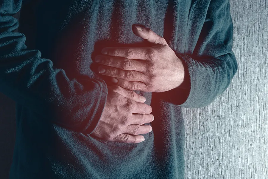 Close-up of the midsection of a man in a green sweater clutching his gut in pain. Get treatment for Ulcerative Colitis from Morgan Burns, APRN in New Smyrna Beach.