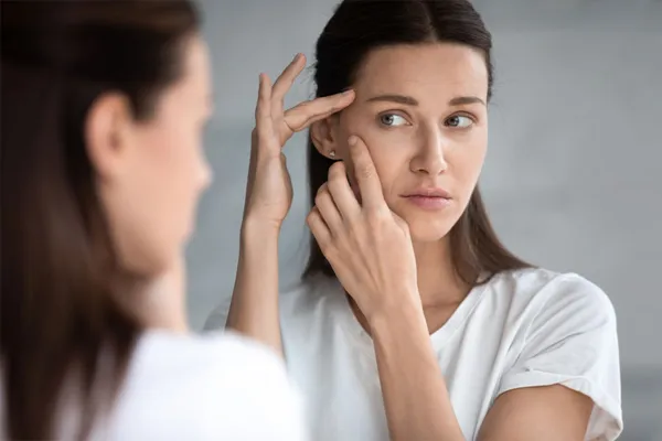 A woman looks at acne in a mirror. Get RF microneedling for acne scar removal from Brandi Terra, NP at Oak & Stone Wellness in San Diego.
