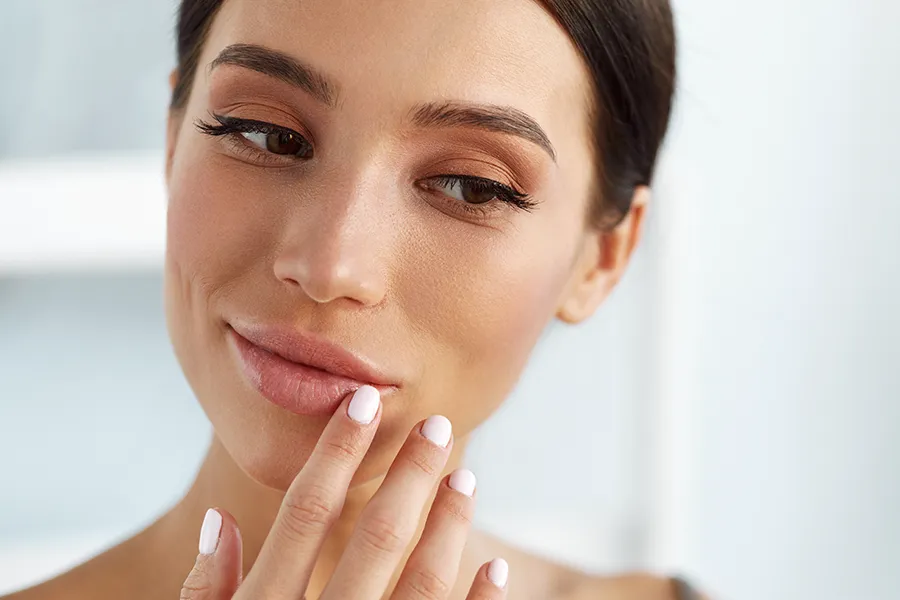 A beautiful brunette touches her faces. Get aesthetic dermal fillers from Brandi Terra, NP at Oak & Stone Wellness in San Diego.