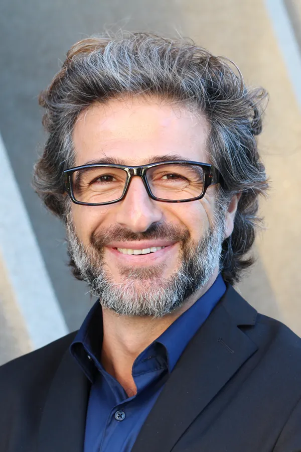 A man with glasses, salt and pepper hair and a beard smiling because he received treatment for andropause and low testosterone from Brandi Terra, NP at Oak & Stone Wellness in San Diego.