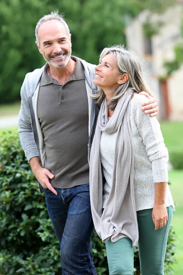 Bioidentical-Hormone-Therapy-Treatment A mature couple in gray toned clothes and jeans walk happily outside, happy with their successful bioidentical hormone treatments from Brandi Terra, NP at Oak & Stone Wellness in San Diego.