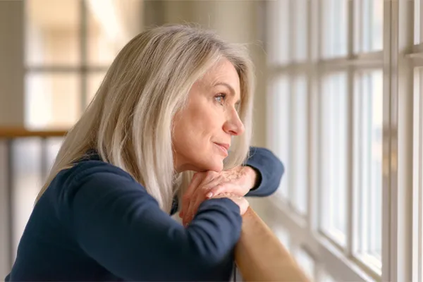 A thoughtful woman gazes out a window, symbolizing the mental fatigue and distraction often associated with brain fog. Get root-cause brain fog treatment by Brandi Terra, NP at Oak & Stone Wellness in San Diego.