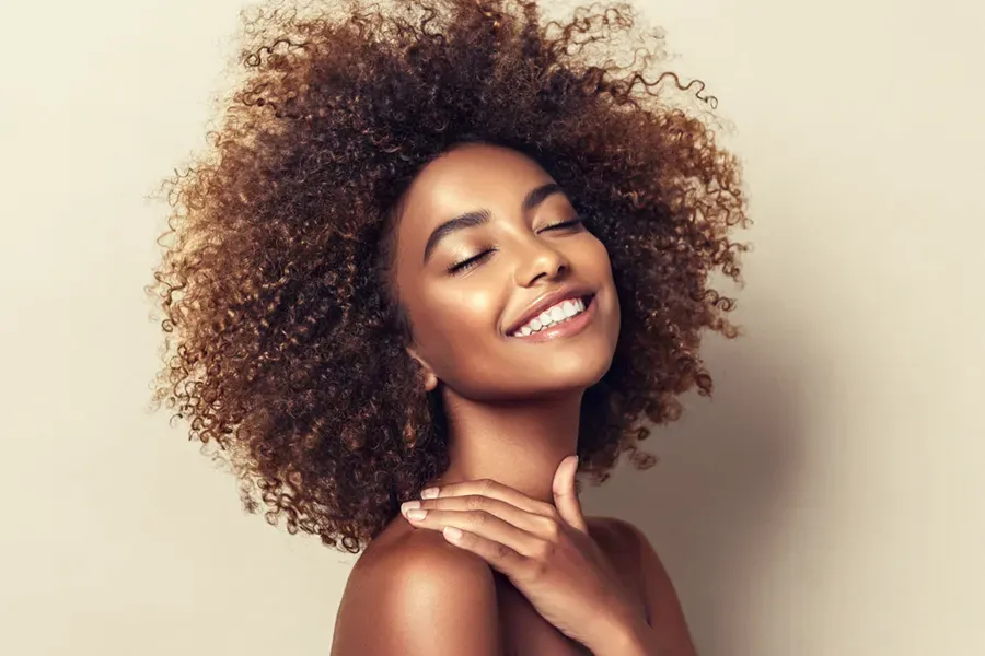 A black woman touches her beautiful smooth skin happily after receiving chemical peel treatments from Brandi Terra, NP at Oak & Stone Wellness in San Diego.