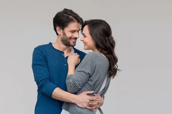 A man in a blue shirt embracing a woman in a gray shirt smiles due to his successful erectile dysfunction care from Brandi Terra, NP at Oak & Stone Wellness in San Diego.