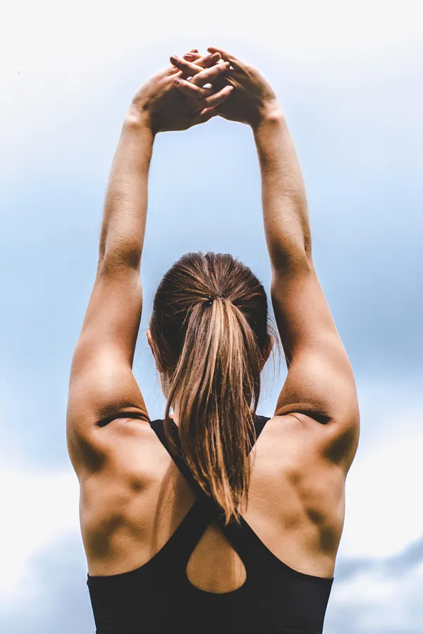A toned woman seen from behind stretching her arms into the air. Get GLP-1 Weight Loss Injections from Brandi Terra, NP at Oak & Stone Wellness in San Diego.