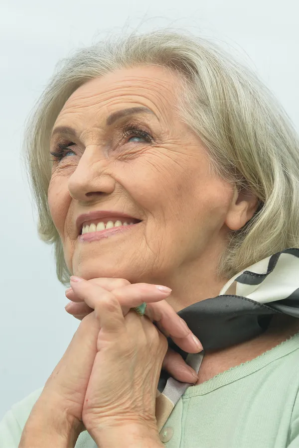 An older woman holds her hands together under her chin and looks up at a cool sky smiling. Get treatment for hot flashes and night sweats from Brandi Terra, NP at Oak & Stone Wellness in San Diego.