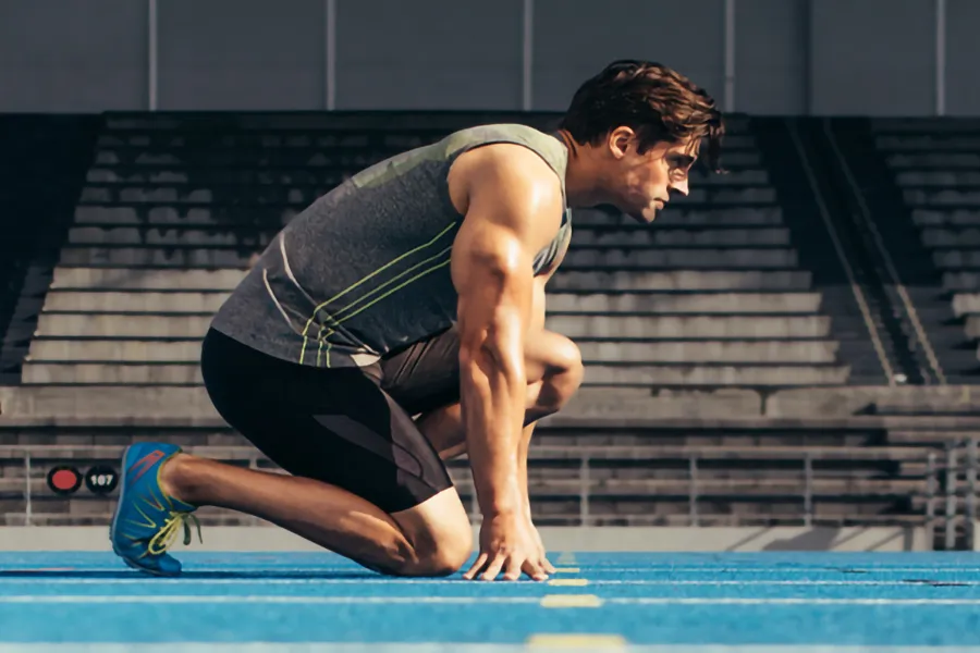 A white man kneels at the starting line on a track, determined to do his best. Get treatment for lean muscle loss and recovery from Brandi Terra, NP at Oak & Stone Wellness in San Diego.