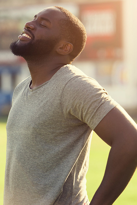 A black man in a gray t-shirt and smiles, looking up with closed eyes after a satisfying workout. Get treatment for lean muscle loss and recovery from Brandi Terra, NP at Oak & Stone Wellness in San Diego.