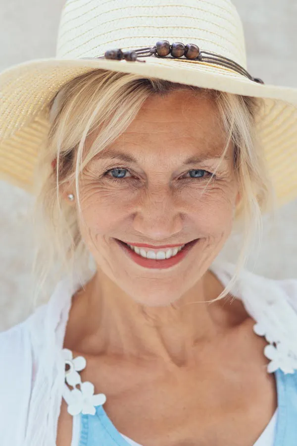A beautiful, smiling older woman with blonde hair and a sunhat, happy with menopause treatment from Brandi Terra, NP at Oak & Stone Wellness in San Diego.