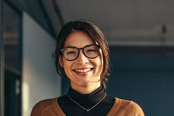 A brunette woman with glasses smiles in a gray-blue walled office. Get metabolic syndrome from Brandi Terra, NP at Oak & Stone Wellness in San Diego.