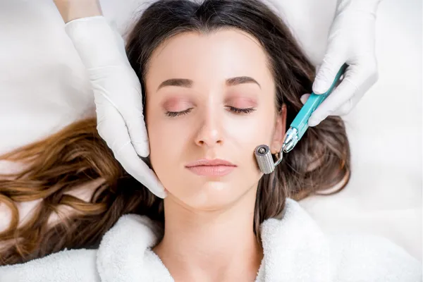 A woman in a white robe closes her eyes and receives a microneedling procedure from Brandi Terra, NP at Oak & Stone Wellness in San Diego.