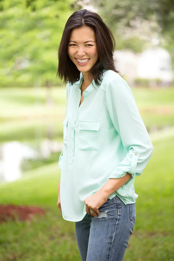 A middle-aged brunette woman in a light green button-up shirt stands outside smiling, happy with her perimenopause treatment from Brandi Terra, NP at Oak & Stone Wellness in San Diego.