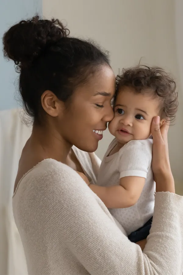 A black woman happily touches her forehead to her infant's head. Get treatment for postpartum hormone imbalance from Brandi Terra, NP at Oak & Stone Wellness in San Diego.