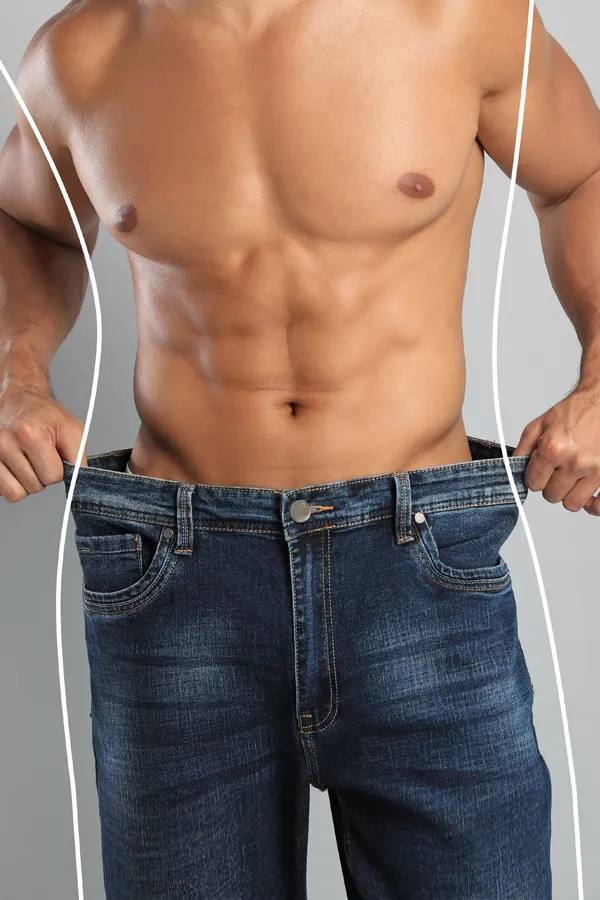 A strong shirtless man in jeans holds the waistlines of his too-big jeans to show the success of semaglutide weight loss from Brandi Terra, NP at Oak & Stone Wellness in San Diego.