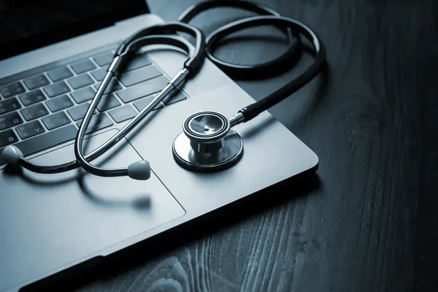 An open laptop with a stethoscope lying on it on a wooden table, symbolizing telemedicine care from Brandi Terra, NP at Oak & Stone Wellness in San Diego.