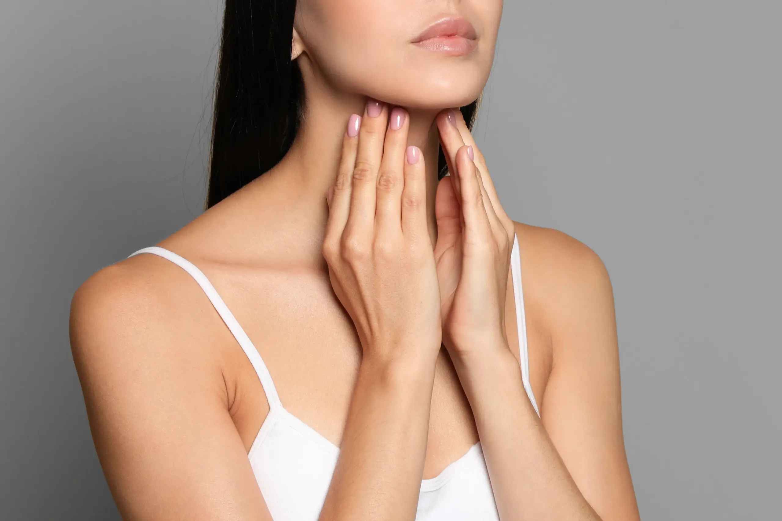 A woman in a white tank top touches her neck looking for signs of thyroid disorder. Get help for thyroid disorders from Brandi Terra, NP at Oak & Stone Wellness in San Diego.