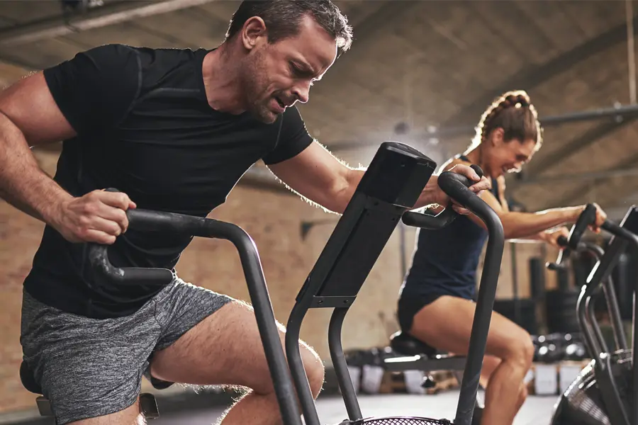 A couple in a brick gym work as hard as they can on exercise bikes, inspired by successful Tirzepatide treatment from Brandi Terra, NP at Oak & Stone Wellness in San Diego.