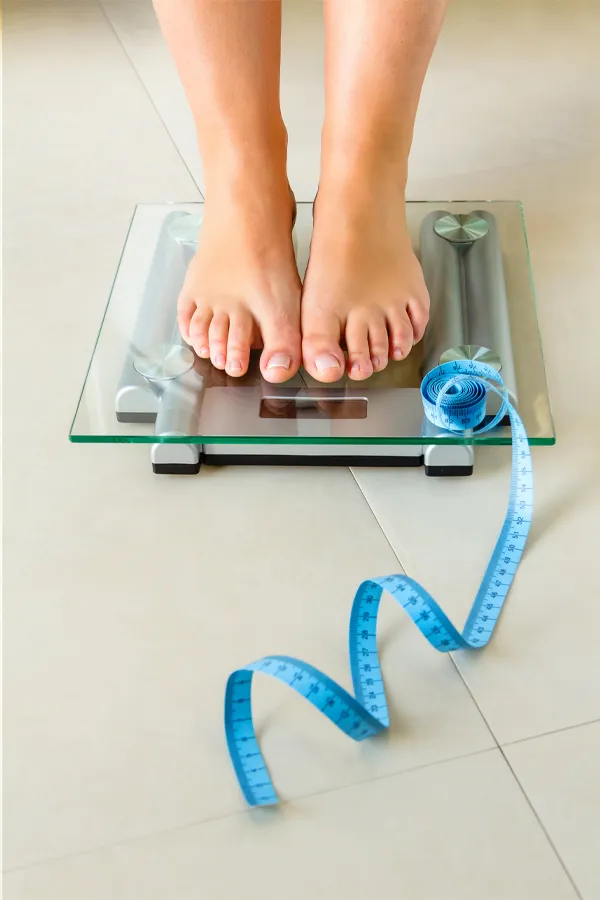 Close-up of a woman's feet standing on a scale, with measuring tape by her toes, getting treatment for weight loss resistance from Brandi Terra, NP at Oak & Stone Wellness in San Diego.