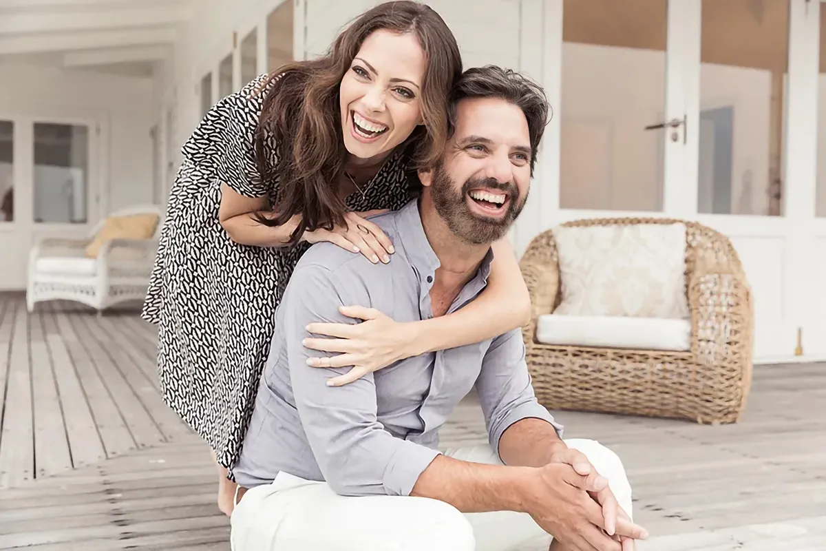 A happy couple embrace on their porch. Get functional medicine treatment from Brandi Terra, NP at Oak & Stone Wellness in San Diego.